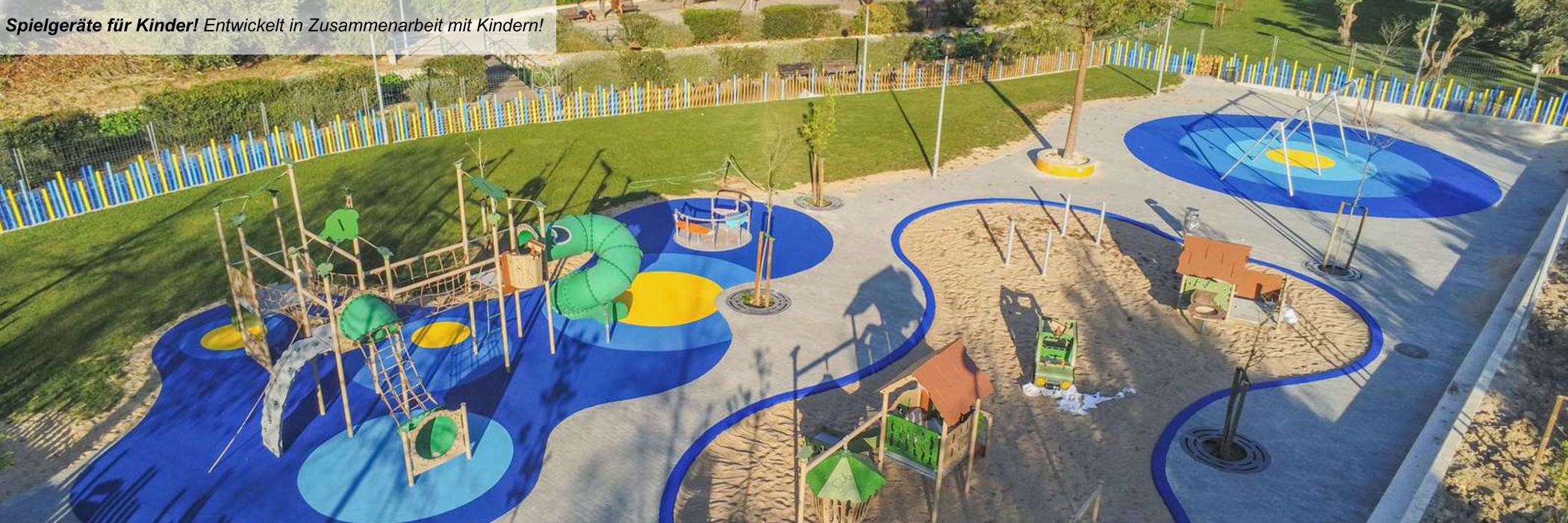 Ein großer Spielplatz mit bunten Flächen, eingezäunt mit einem bunten Gartenzaun inmitten einer Wohnanlage